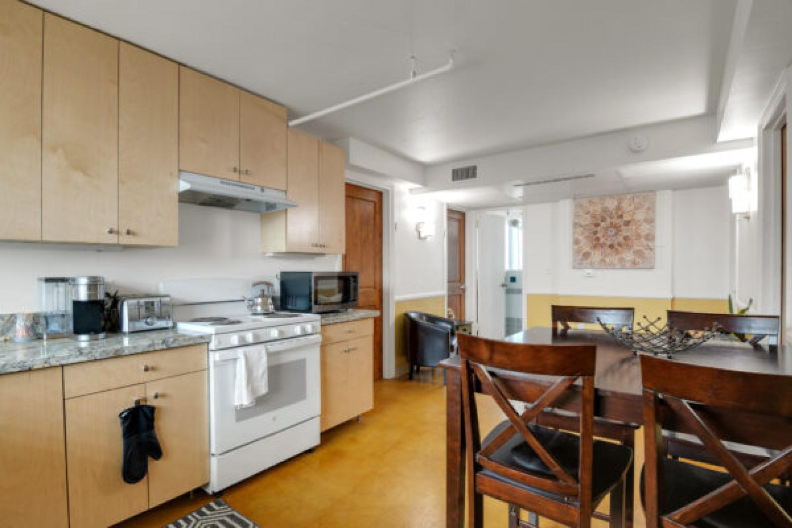 Contemporary kitchen with light wood cabinets, granite counters, white appliances, and a dining area with dark wood table and chairs.