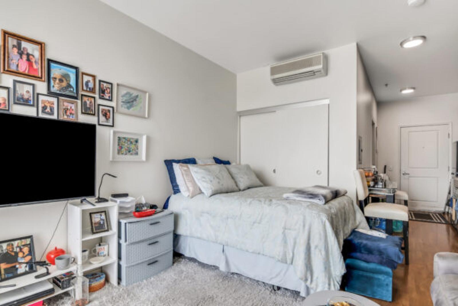 Cozy studio bedroom with a queen bed, wall-mounted TV, gallery wall, and white sliding wardrobe doors.