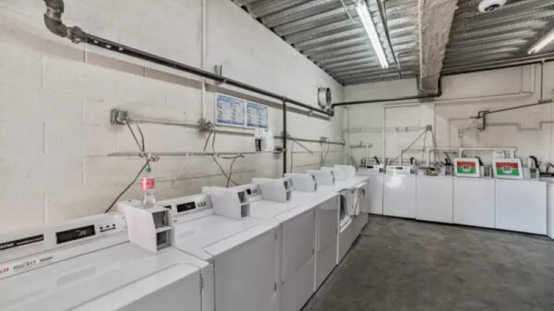 Rows of white washing machines and dryers in a bright, industrial-style laundromat.