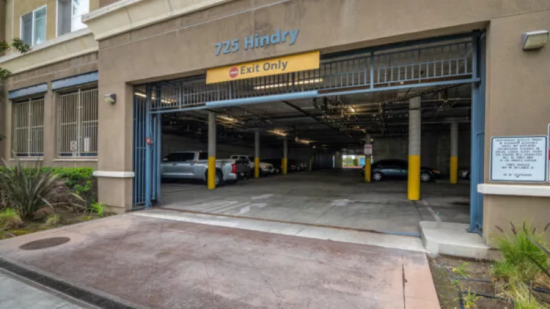 Entrance to a parking garage with a "775 Hindry" sign and "Exit Only" marking, cars visible inside.