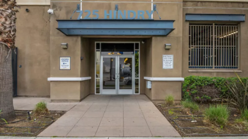 Tan commercial building entrance with glass doors. Blue lettering "725 HINDRY" is above a dark blue canopy.