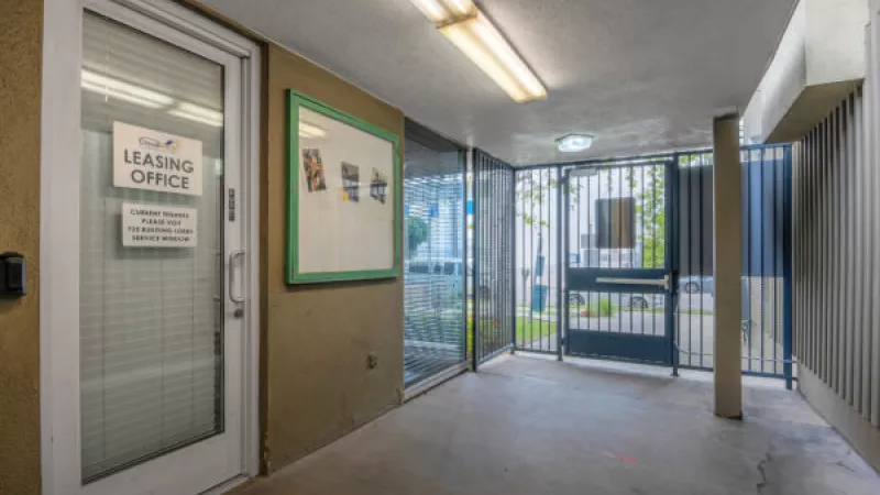 Entrance to a leasing office with a glass door on the left and a dark metal gate leading to an outdoor area on the right.