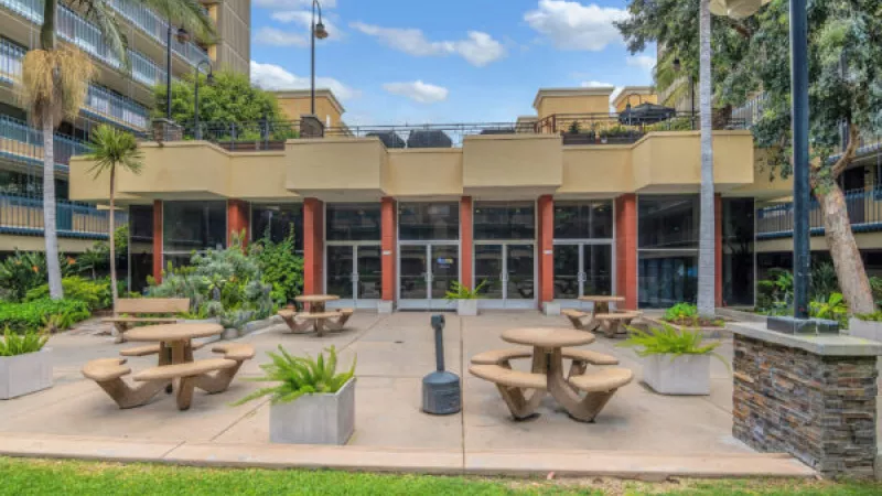 Outdoor courtyard with beige picnic tables, a building with large windows, and residential towers.