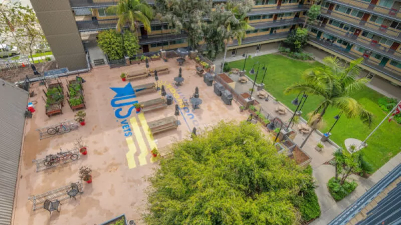 Aerial view of a university courtyard with a blue and yellow "CSUN" graphic, benches, trees, and surrounding buildings.