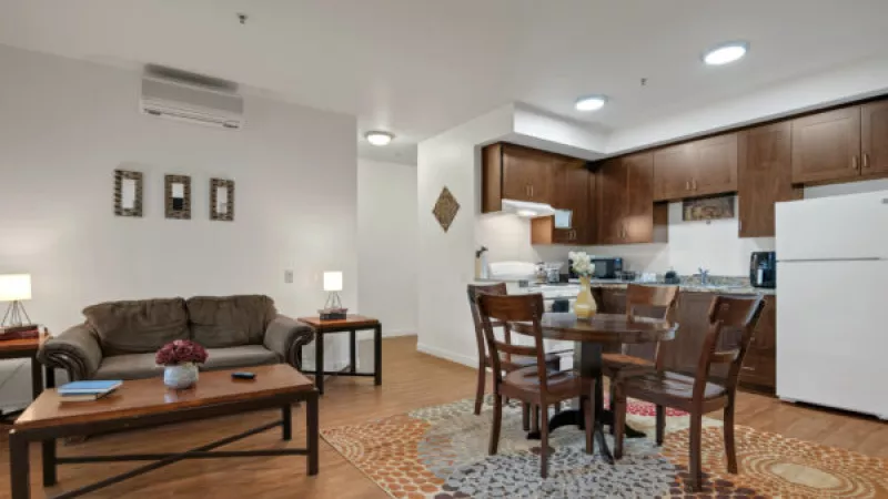 Modern apartment: living room with brown sofa, dining area with round table, and dark wood kitchen cabinets.