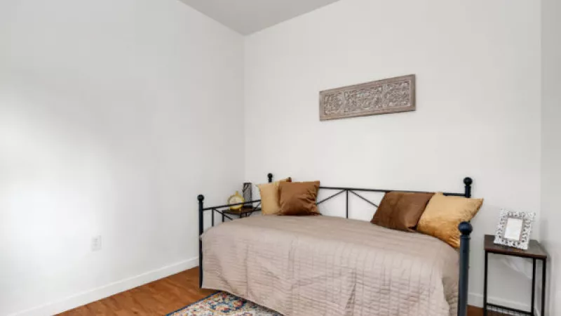 Bedroom with white walls, wood floor, black daybed with brown bedding, and a colorful patterned rug. Decorative wall art.