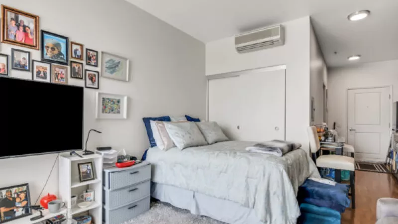 Cozy studio bedroom with a queen bed, wall-mounted TV, gallery wall, and white sliding wardrobe doors.