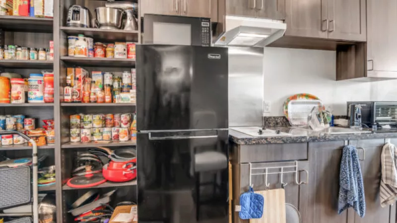 Kitchen with a large, well-stocked pantry, black refrigerator, microwave, and dark cabinets over a counter with a stove.