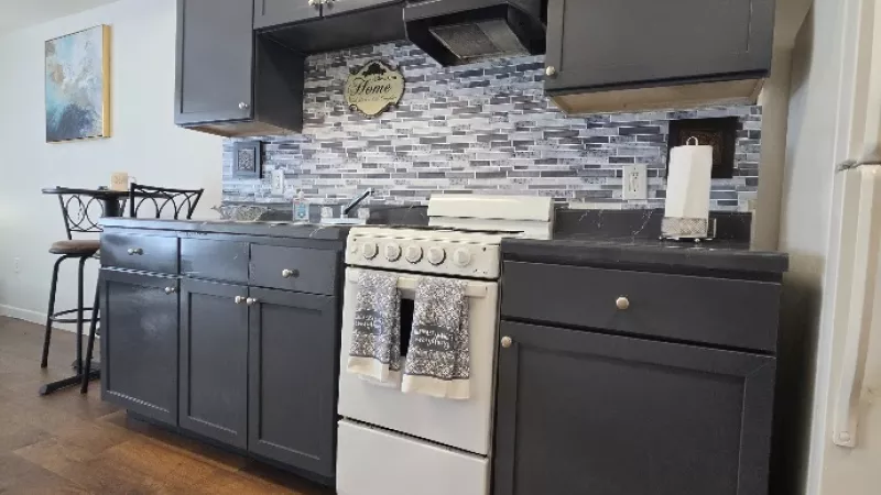 Small kitchen with dark gray cabinets, white stove, tiled backsplash, wooden floor, and a white refrigerator.
