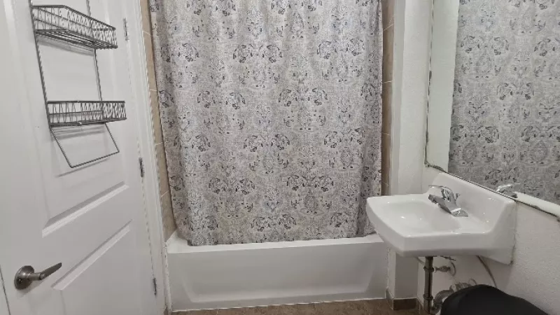 Small bathroom with a white patterned shower curtain, sink, mirror, and brown tiled floor.