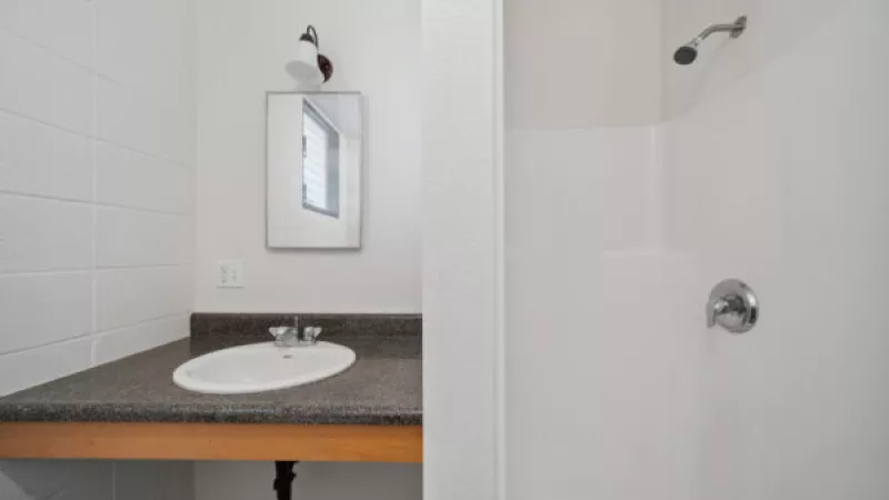 Bathroom with a white sink on a dark counter, a mirror, and a white shower stall with silver fixtures.