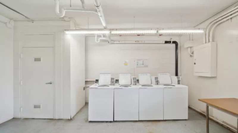 Clean utility room with four white front-loading laundry machines, a closed door, concrete floor, and a wooden table.