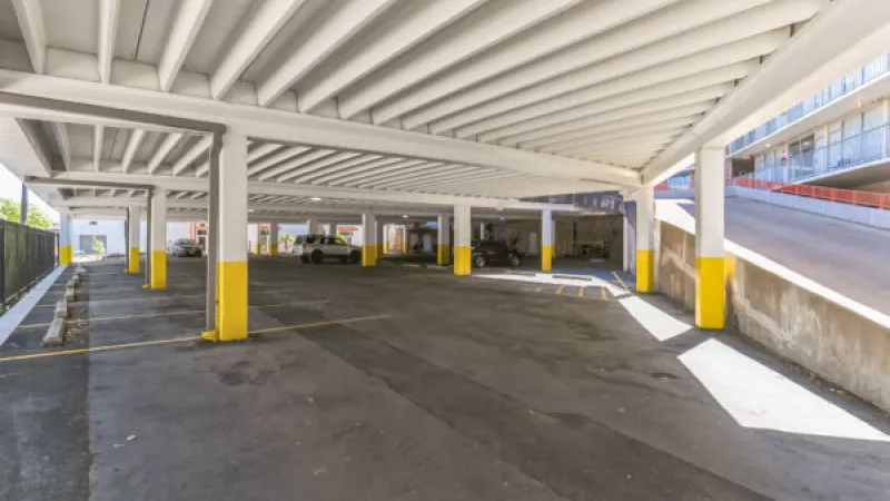 Empty covered parking garage with concrete support columns, some painted yellow at the base.