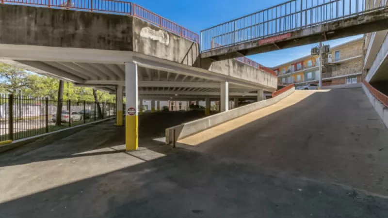 Multi-level concrete parking garage with yellow support pillars, red railings, and ramps, under a clear blue sky.
