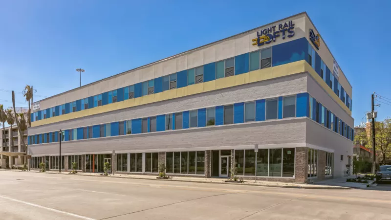 Long, modern gray building with blue windows and yellow trim, displaying "Heritage Pointe" and "Heritage Hotel" logos.