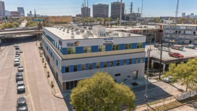 Aerial view of a modern grey and blue commercial building with an orange and white logo, in an urban setting.