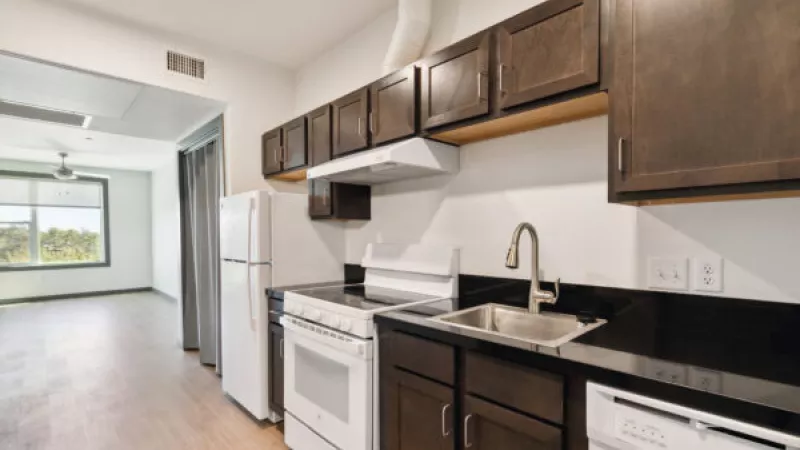 Modern kitchen with dark cabinets, black counters, white appliances, and a view into an open living room.
