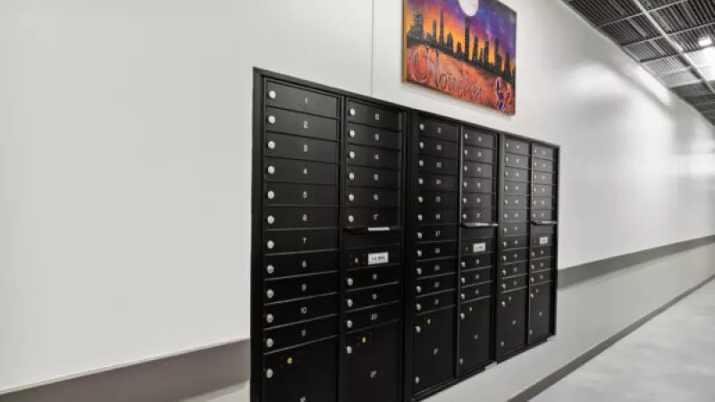 Black mailboxes with gold locks line a white hallway. A vibrant city skyline painting under a full moon hangs above them.