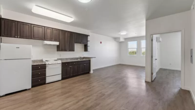 Spacious, unfurnished open-plan apartment with a kitchen featuring dark wood cabinets, white appliances, and wood floors.