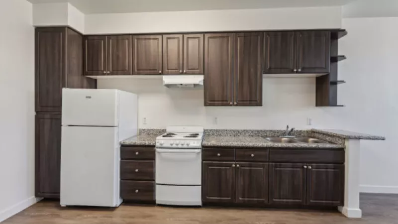 Modern kitchen with dark brown cabinets, speckled granite counters, white refrigerator and stove, and wood-look floor.