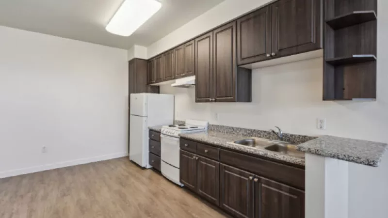 Empty kitchen with dark wood cabinets, granite countertops, white appliances, and light wood flooring.