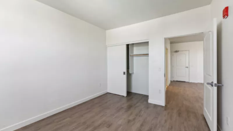 Unfurnished room with white walls, wood flooring, an open closet, and a doorway leading to a hall.