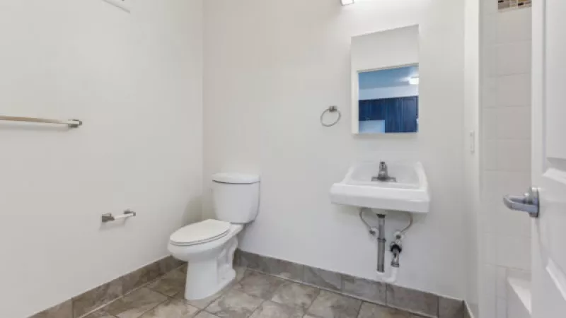 Clean white bathroom with a toilet, wall-mounted sink, mirror, overhead light, and tiled floor.