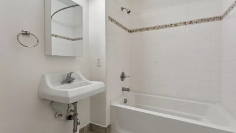 Small, white bathroom with a sink, mirror, and bathtub. Tiled walls and floor.