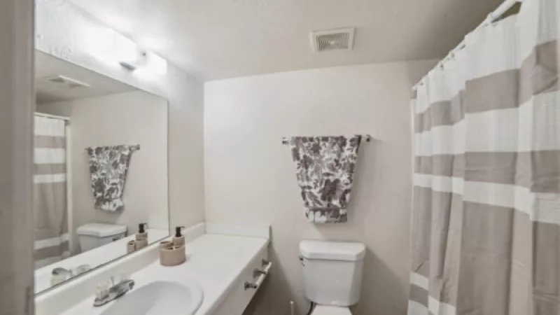 Clean bathroom with white vanity, sink, mirror, toilet, and striped brown and white shower curtain.