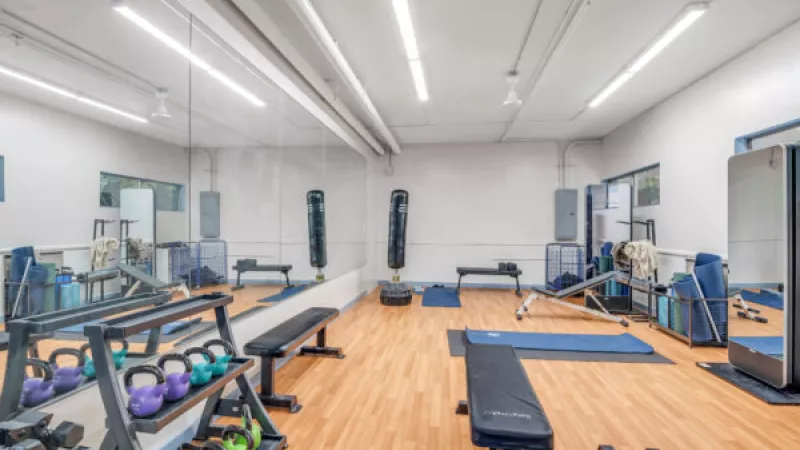 Clean, bright gym with a mirrored wall, racks of colorful weights, benches, a punching bag, and exercise mats.