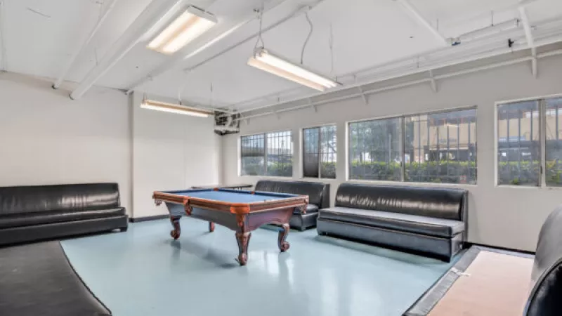 Recreation room with a blue-felt pool table, black leather couches, and windows along one wall.