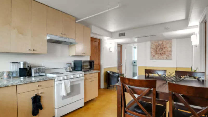 Contemporary kitchen with light wood cabinets, granite counters, white appliances, and a dining area with dark wood table and chairs.
