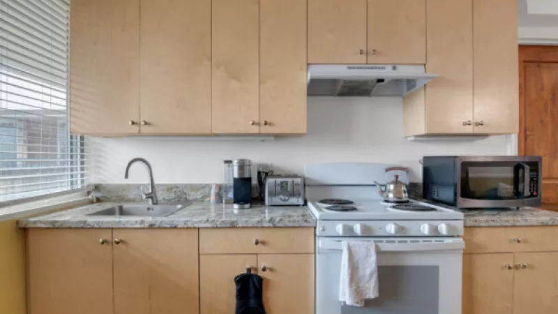 Modern kitchen with light wood cabinets, granite counters, white stove, microwave, and sink by a window.