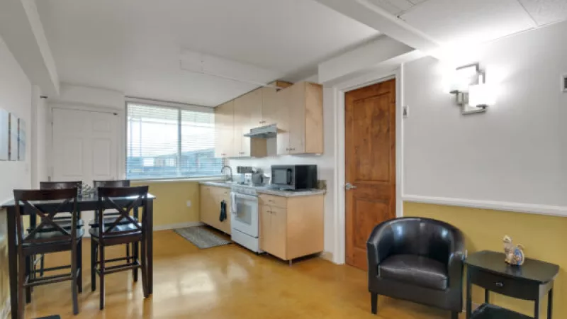 Open-plan kitchen and dining with light wood cabinets, dark dining set, yellow floor, and a brown leather armchair.