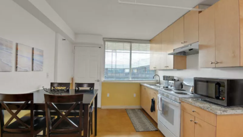 Bright kitchen and dining area with light wood cabinets, white appliances, dark dining table, and a window.