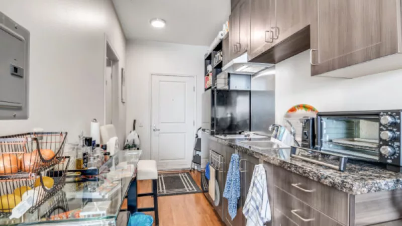 Modern kitchen with gray cabinets, dark granite counters, various appliances, and a white door in the background.