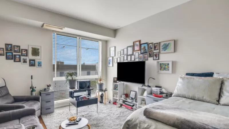 Photograph of a bright studio apartment with a bed, gray sofa, desk, and many framed photos.