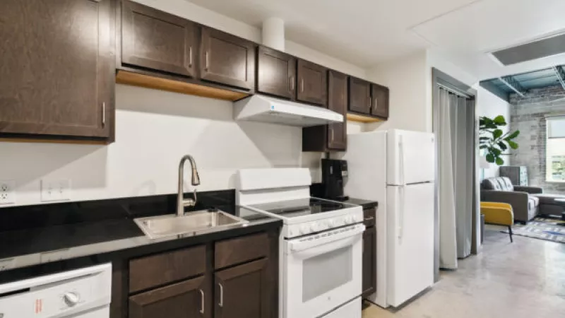 Modern kitchen with dark brown cabinets, black countertops, white appliances, and an open layout to a living area.