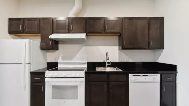 Modern kitchen with dark brown cabinets, black countertops, and white appliances: refrigerator, stove, and dishwasher.
