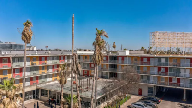 Colorful apartment community with palm trees, courtyard, and parked cars under a blue sky.