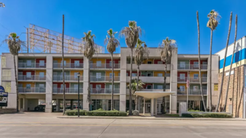 White apartment community with vibrant red, green, and yellow balconies, tall palm trees, and a clear blue sky.