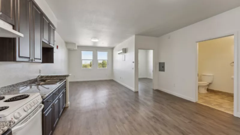 Unfurnished apartment with dark kitchen cabinets, white stove, granite counters, wood-look floors, and bathroom.