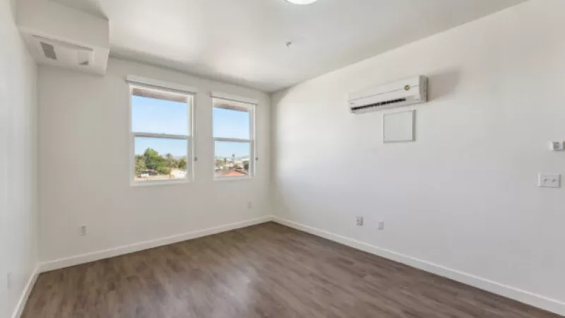 Empty room with white walls, wood laminate floor, two windows, and two wall-mounted AC units.