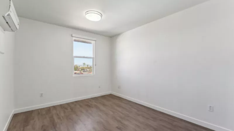 Empty room with white walls, wood-grain floor, a window overlooking trees, and a wall-mounted air conditioning unit.