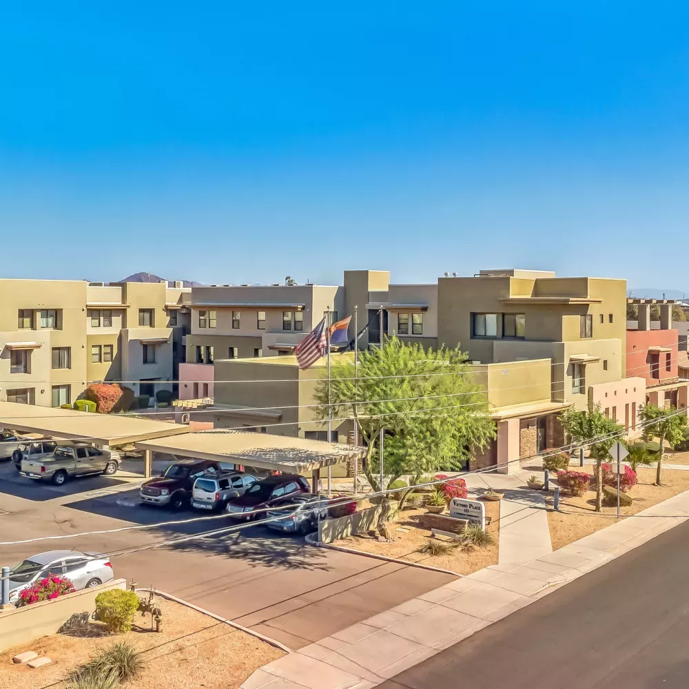 Aerial view of a modern tan apartment complex with colored accents, covered parking, and a clear blue sky.