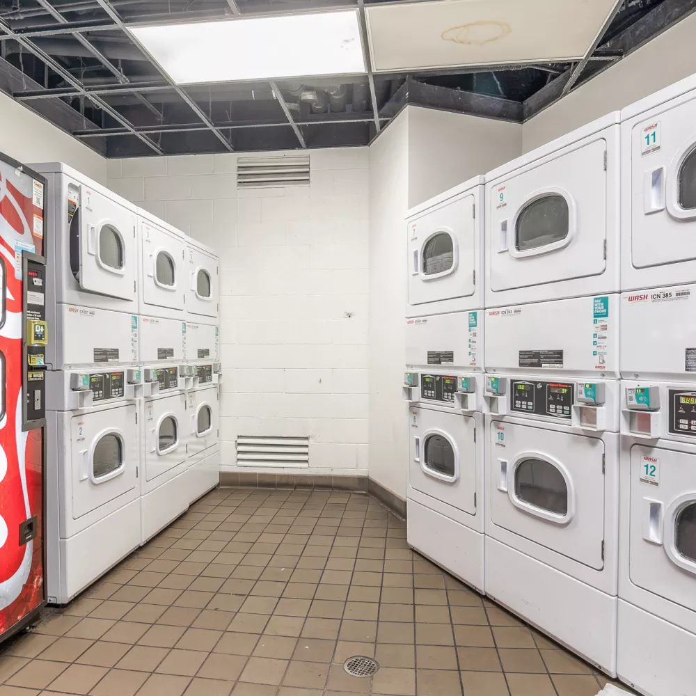 A small laundry room with a red Coca-Cola vending machine and rows of white washing machines and dryers.