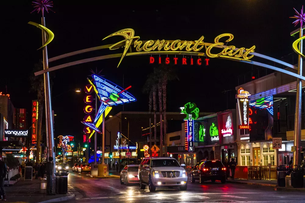  Fremont East District in Las Vegas at night. A neon archway, colorful signs, and cars illuminate the street.