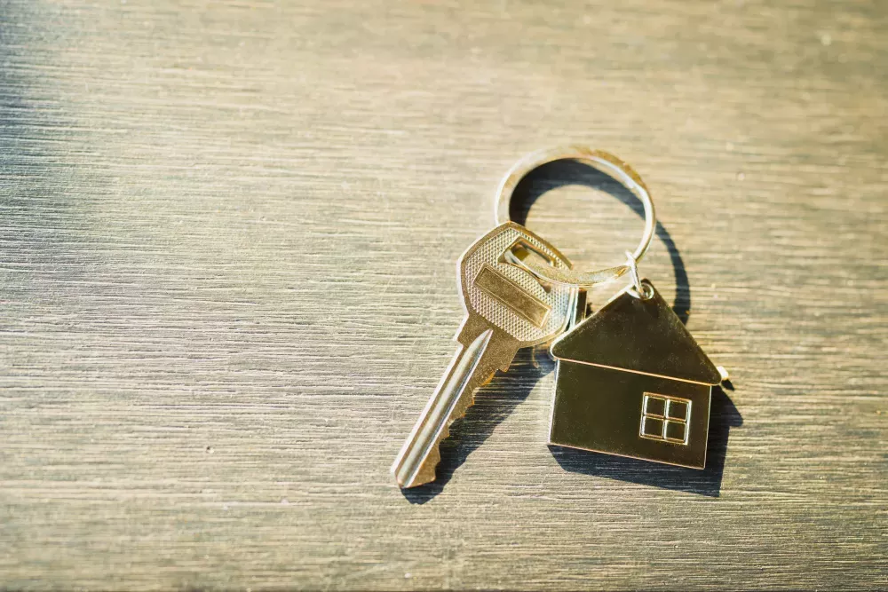 Silver house keys with a small house charm, resting on a textured wooden background.
